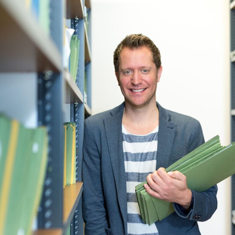 Dirk Hermens in het archief met mappen in zijn handen.